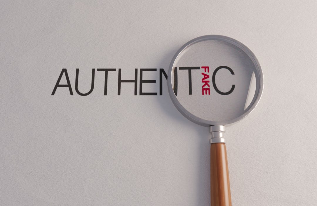A counterfeit concept of a magnifying glass on white surface showing the word fake hidden in the word authentic