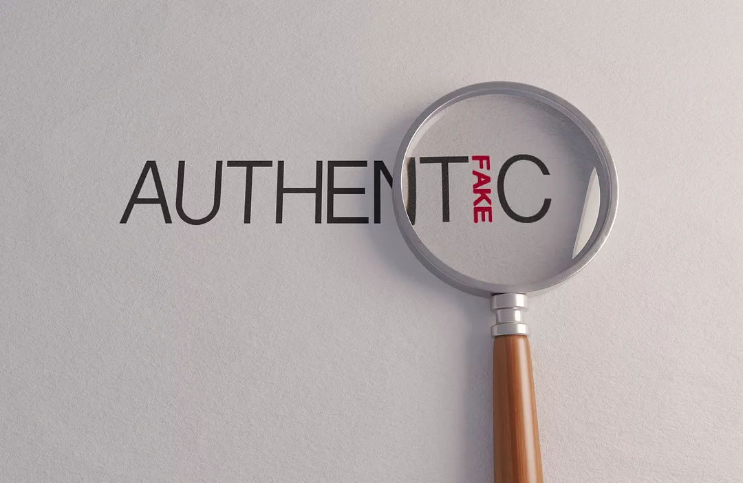 A counterfeit concept of a magnifying glass on white surface showing the word fake hidden in the word authentic
