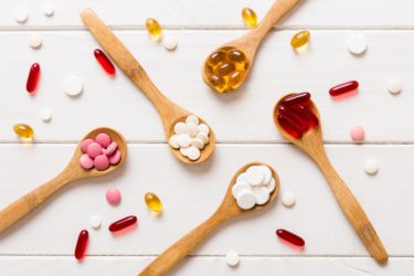 Vitamin capsules in a spoon on a colored background. Red soft gel vitamin supplement capsules on spoon.
