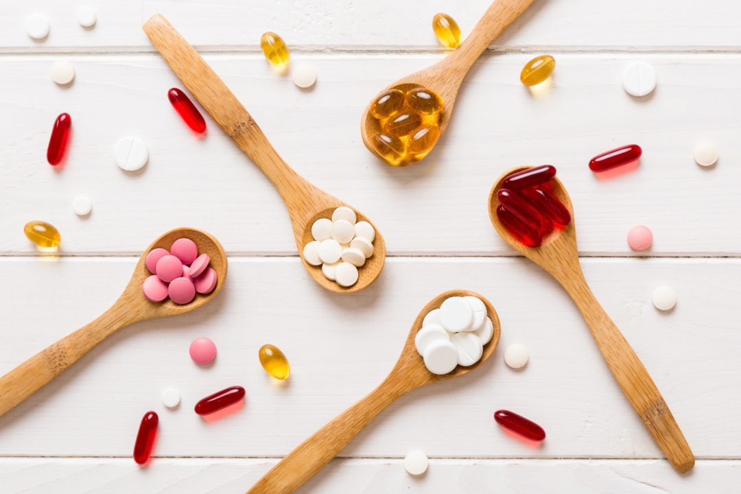 Vitamin capsules in a spoon on a colored background. Red soft gel vitamin supplement capsules on spoon.