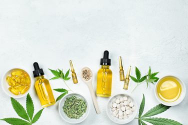 cbd oil, ampoules, capsules and tablets with cannabidiol and cannabis leaves on gray concrete table