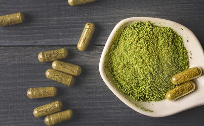 Top view of Kratom powder in ceramic spoon and Kratom capsules on wooden table.
