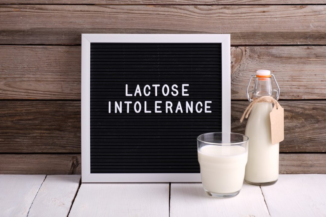 Allergic food concept. Milk bottle, milk glass and letter board with text LACTOSE INTOLERANCE on wooden background.