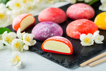 Multi-colored Japanese ice cream Mochi in rice dough and Jasmine flowers on a concrete blue background.