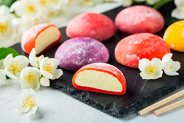 Multi-colored Japanese ice cream Mochi in rice dough and Jasmine flowers on a concrete blue background.