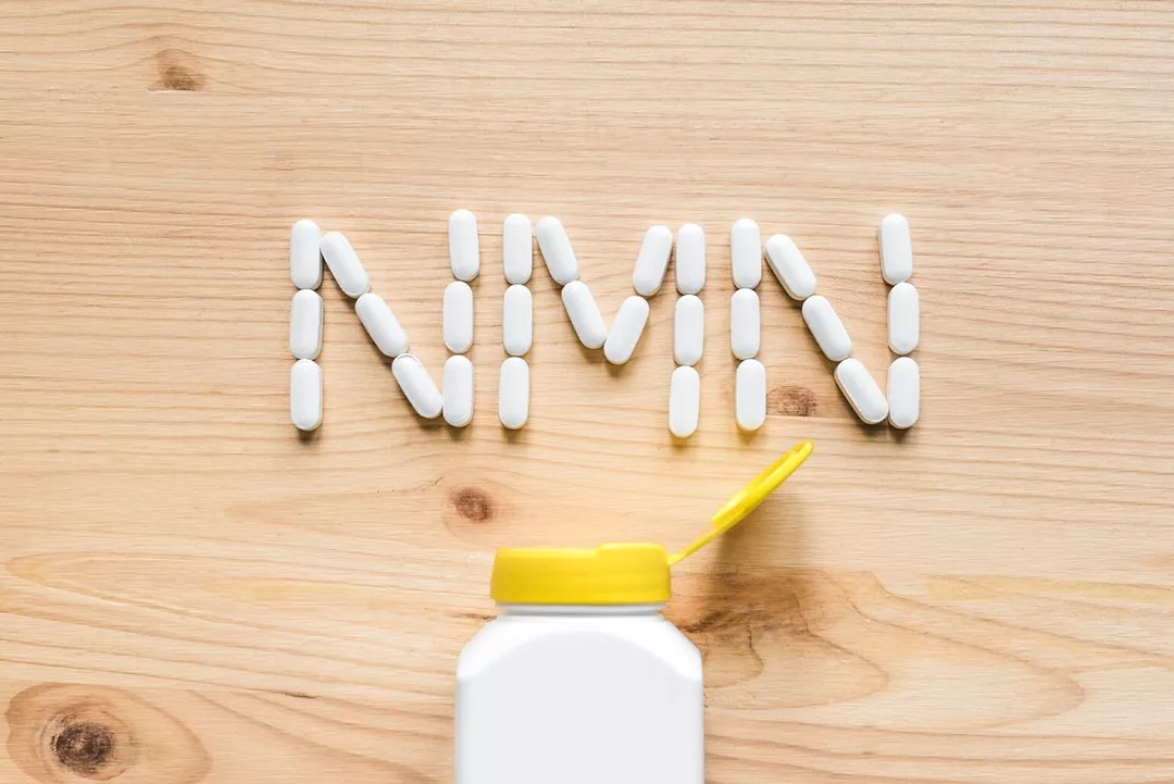 Nicotinamide mononucleotide, niacin, anti adeing vitamin. White pills forming shape to NMN alphabet on wooden background, copy space, top view.
