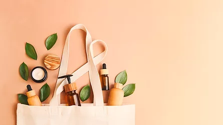 Open eco friendly cotton reusable bag with different containers from natural wood and brown glass.Fresh leafs around.Concept of organic,zero waste cosmetics.