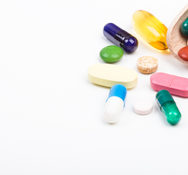 Various color pills and capsules with wooden dispenser on white background