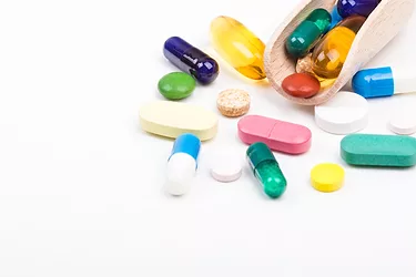 Various color pills and capsules with wooden dispenser on white background