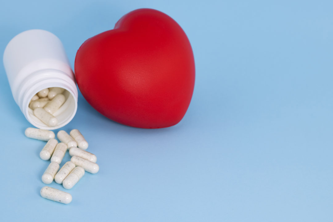 white pills spilling out of bottle and red heart on a blue background.