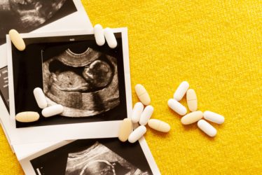 Photos of the fetus on ultrasound scan and few pills on yellow background.Vitamins and proper nutrition for a pregnant woman. 
