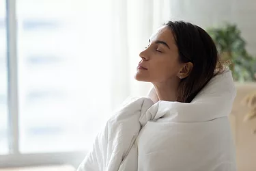 Calm woman wrapped in blanket relax breathing fresh air at home, rest meditate, indoors, stress free concept