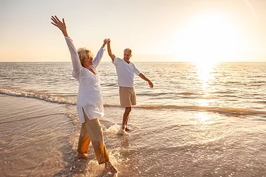 Happy senior man and woman old retired couple walking and holding hands on a beach at sunset.
