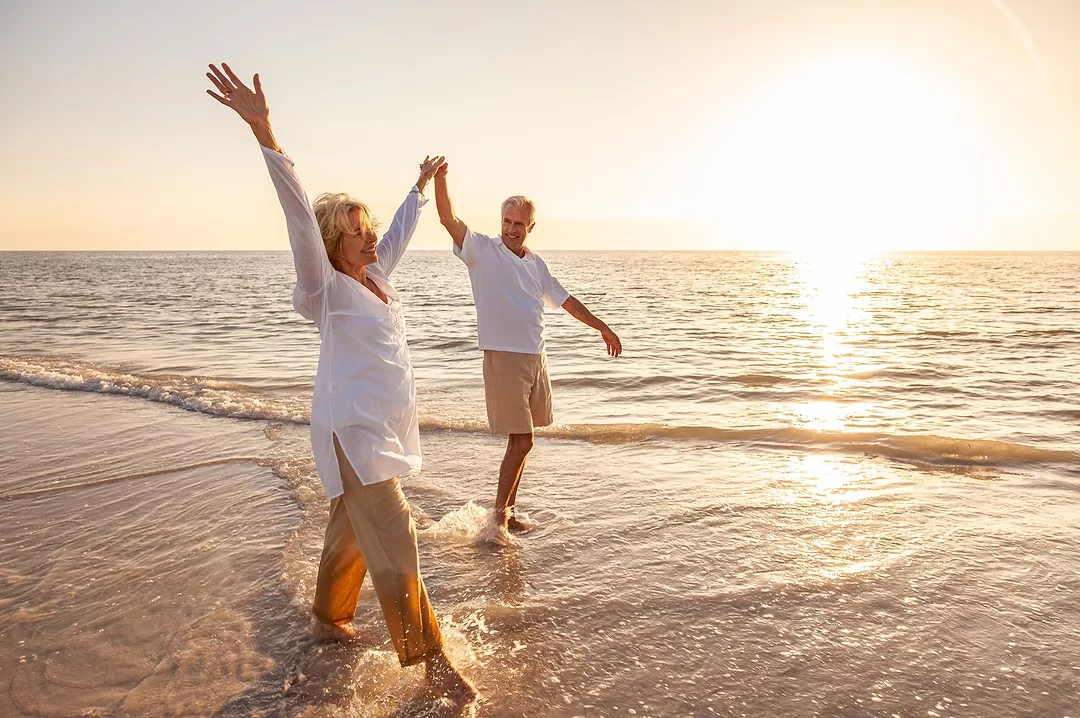 Happy senior man and woman old retired couple walking and holding hands on a beach at sunset.
