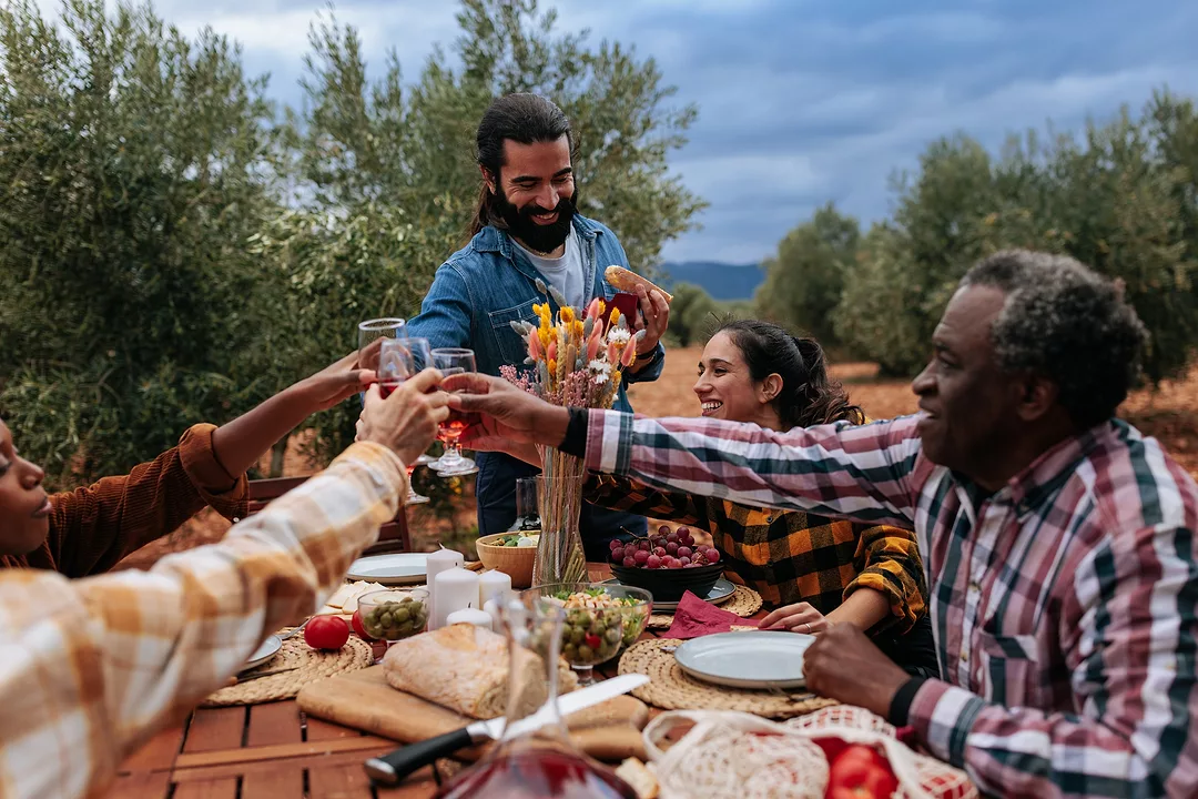 Group enjoying a meal and toasting with wine at a table set outdoors in an olive grove