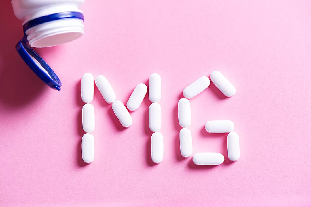 Mineral pill capsule Magnesium. White vitamin pills forming shape to Mg sign and plastic bottle on pink background, top view.