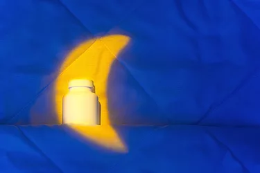 Bottle of melatonin supplements in moon set on blanket in bed.
