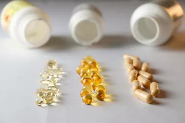 Various colored capsules and soft gels are laid out in a neat arrangement beside several opened supplement bottles.