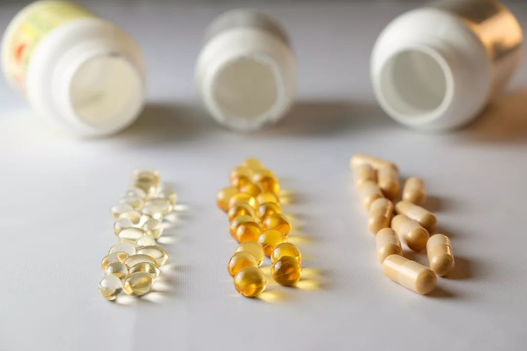 Various colored capsules and soft gels are laid out in a neat arrangement beside several opened supplement bottles.
