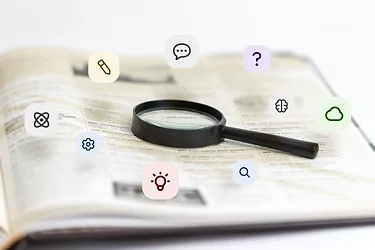 Research-gettyImages-2184422669.jpg Magnifying glass over book with floating icons: atoms, pencils, ideas, dialogue bubbles. Education, research, knowledge.