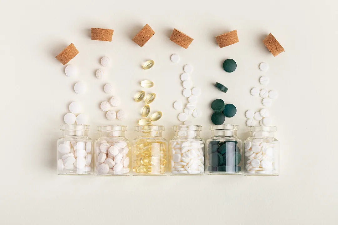 Assorted dietary supplements, including capsules, tablets, softgels, and vitamins, displayed in bowls and bottles.